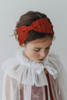 A young girl is wearing a red dress with a white tulle cape adorned with embroidered red roses. The floral details of her ensemble are striking. The shades of red and green are the perfect addition to our Red Rose Princess Collection.