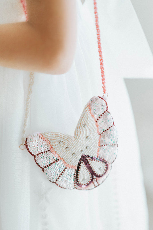 Girls’ butterfly-shaped beaded purse with sequin wings and pink strap, styled with an elegant white dress
Delicate butterfly crossbody purse with beaded wings and sparkle detail, perfect for dress-up or special occasions
Iridescent butterfly beaded bag hanging from a girl's shoulder, styled with embroidered white gown
Whimsical sequin butterfly purse for girls with pink and pearl beading, ideal for weddings or birthday dress-up