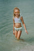 Girl wearing mint green mermaid swimsuit with purple seashell top and gold waistband, standing at the shoreline in fun sunglasses
Mermaid-themed ruffle bikini for girls with shell applique and scale print bottoms, styled for beach photos and play
Child in seafoam green two-piece swimsuit with frilly straps and shell detail, posing on sandy beach in sunshine