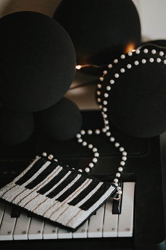 Hand-beaded black and white piano clutch with gold accents and pearl strap, styled on a keyboard for musicians, concert accessories, or music-themed gifts.
Elegant piano key beaded clutch purse with pearl shoulder strap, featuring black and white seed beads and gold shimmer, ideal for recitals or evening events.
Black and white piano beaded purse resting on piano keys, with pearl crossbody strap, styled for music lovers and formal holiday or recital nights.