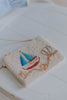 White beaded purse with embroidered sailboat and rope accents, styled for toddler or child’s coastal vacation or seaside photos
Girls’ beaded sailboat handbag with nautical design, shown with blue summer outfit for beach or boat day styling
Hand-beaded crossbody purse with colorful sailboat design, ideal for ocean-themed accessories, toddler travel, or beach outfits