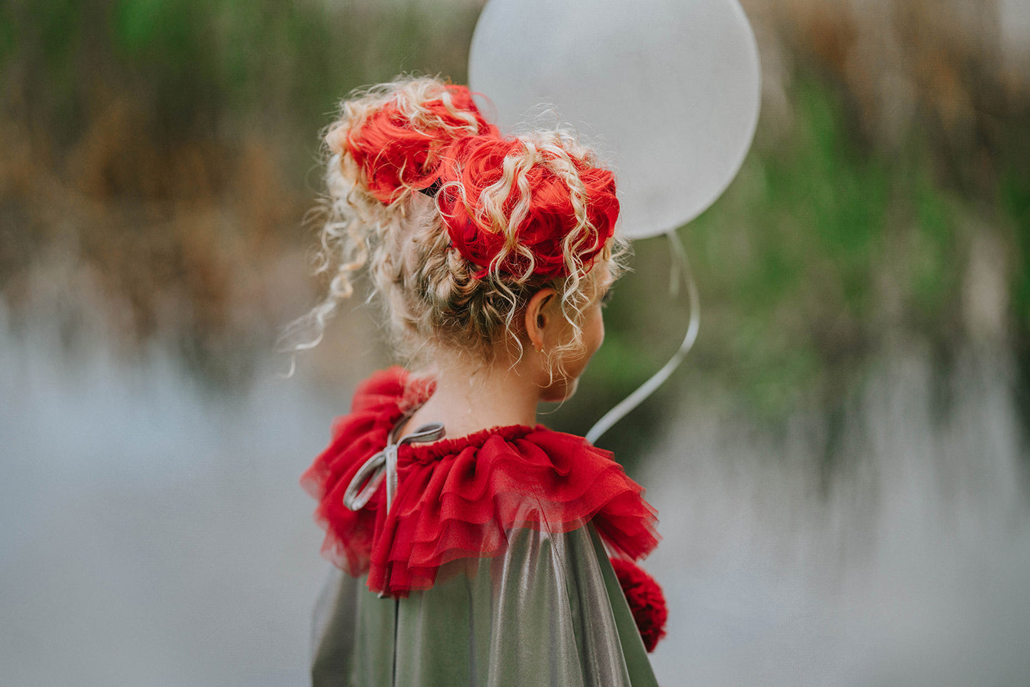 Dancing clown costume for girls in shiny silver and red with dramatic pom-poms and a layered ruffle neckline, perfect for dress-up
Young girl in vintage circus-inspired clown dress holding a balloon, wearing metallic cape with red trim and curly hair buns
Theatrical clown costume for kids with metallic silver fabric and bold red accents, ideal for Halloween or costume party photos