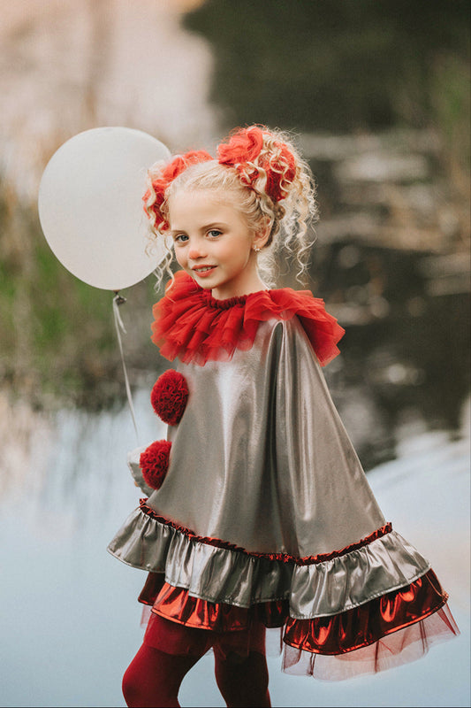Girl wearing silver and red clown costume with ruffled collar and pom-poms, holding a white balloon near a pond in whimsical setting
Child dressed in metallic clown cape with red tights and tulle ruffle collar, styled for Halloween or circus-themed photoshoot
Dancing clown costume for girls in shiny silver and red with dramatic pom-poms and a layered ruffle neckline, perfect for dress-up
