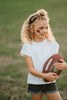 Girl wearing black “Go Blue” headband holding football on grassy field, dressed in white tee and denim shorts for game day
Child showing school spirit in sparkly “Go Blue” headband and football face sticker, styled for sports team support
Little girl wearing team pride headband that says “Go Blue” while smiling and holding a Wilson football outdoors
Blonde girl in football fan outfit with “Go Blue” headband and face paint, standing on a green field during sunset