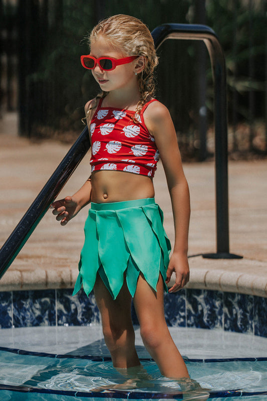 Girl wearing red monstera crop top and green leaf skirt swimsuit standing by the pool in tropical-themed two-piece swimwear
Toddler girl in Hawaiian two-piece swimsuit with red monstera print top and layered green leaf skirt at the poolside
Child in tropical swim outfit with red printed crop top and green leaf petal skirt, styled for luau or summer vacation