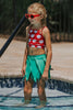 Girl wearing red monstera crop top and green leaf skirt swimsuit standing by the pool in tropical-themed two-piece swimwear
Toddler girl in Hawaiian two-piece swimsuit with red monstera print top and layered green leaf skirt at the poolside
Child in tropical swim outfit with red printed crop top and green leaf petal skirt, styled for luau or summer vacation