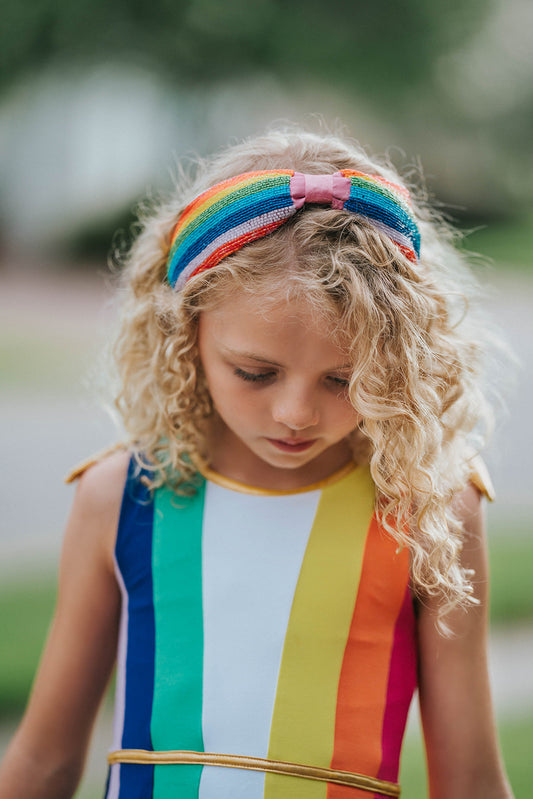 Soft fabric-covered headband featuring a pastel rainbow design in pink, yellow, mint, and lavender hues. Designed for children, with a comfortable fit and gentle grip for everyday wear or coordinating with dress-up outfits.
