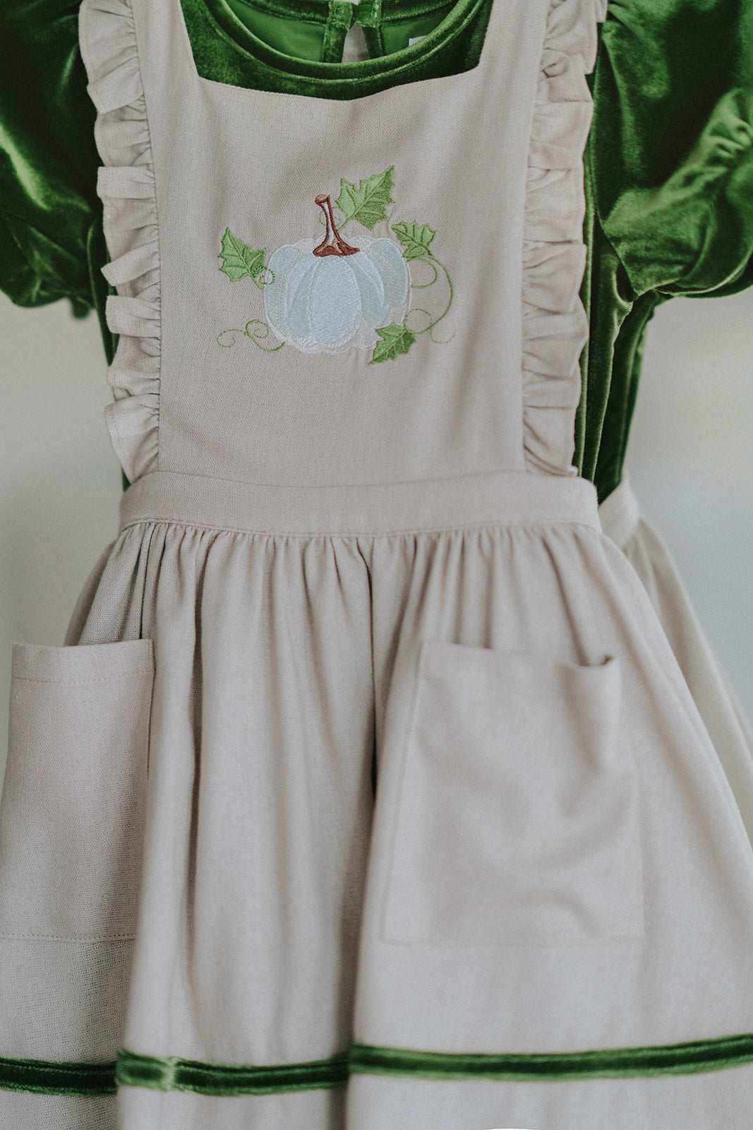 Heirloom-style green velvet holiday dress with linen pinafore and pumpkin embroidery, styled for autumn or fairytale dress-up
Fall girls outfit with green velvet dress and embroidered pumpkin apron, hanging on vintage white carved mirror
Toddler to tween Thanksgiving dress with velvet base, apron pockets, and embroidered pumpkin design, ideal for family photos
Girls embroidered apron dress with green velvet and ruffle-trimmed linen pinafore, perfect for pumpkin patch or harvest festival