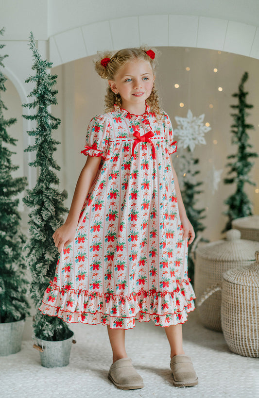 Vintage-style girls Christmas nightgown with red bows, holly print, ruffle trim, and satin bow, hanging on a carved white mirror
Classic holiday pajama dress for girls with red and green holly print, ruffle hem, and red satin bow at the neckline
Girls long sleeve Christmas nightgown with festive red bow and holly pattern, styled for holiday photos or heirloom gifting
Traditional girls holiday nightgown in white with red an
