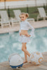 Young girl modeling a space princess-themed rash guard swim set by a pool. The outfit features a white long-sleeve crop top with flared cuffs and a high neckline, paired with a matching flared swim skirt adorned with silver button details. Her blonde hair is styled in iconic double buns, inspired by a classic sci-fi look. Star Wars-themed inflatable droids are placed nearby, enhancing the playful galactic vibe.