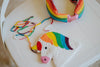 Rainbow unicorn-shaped beaded handbag for kids with colorful strap, shown with matching headband on chair
