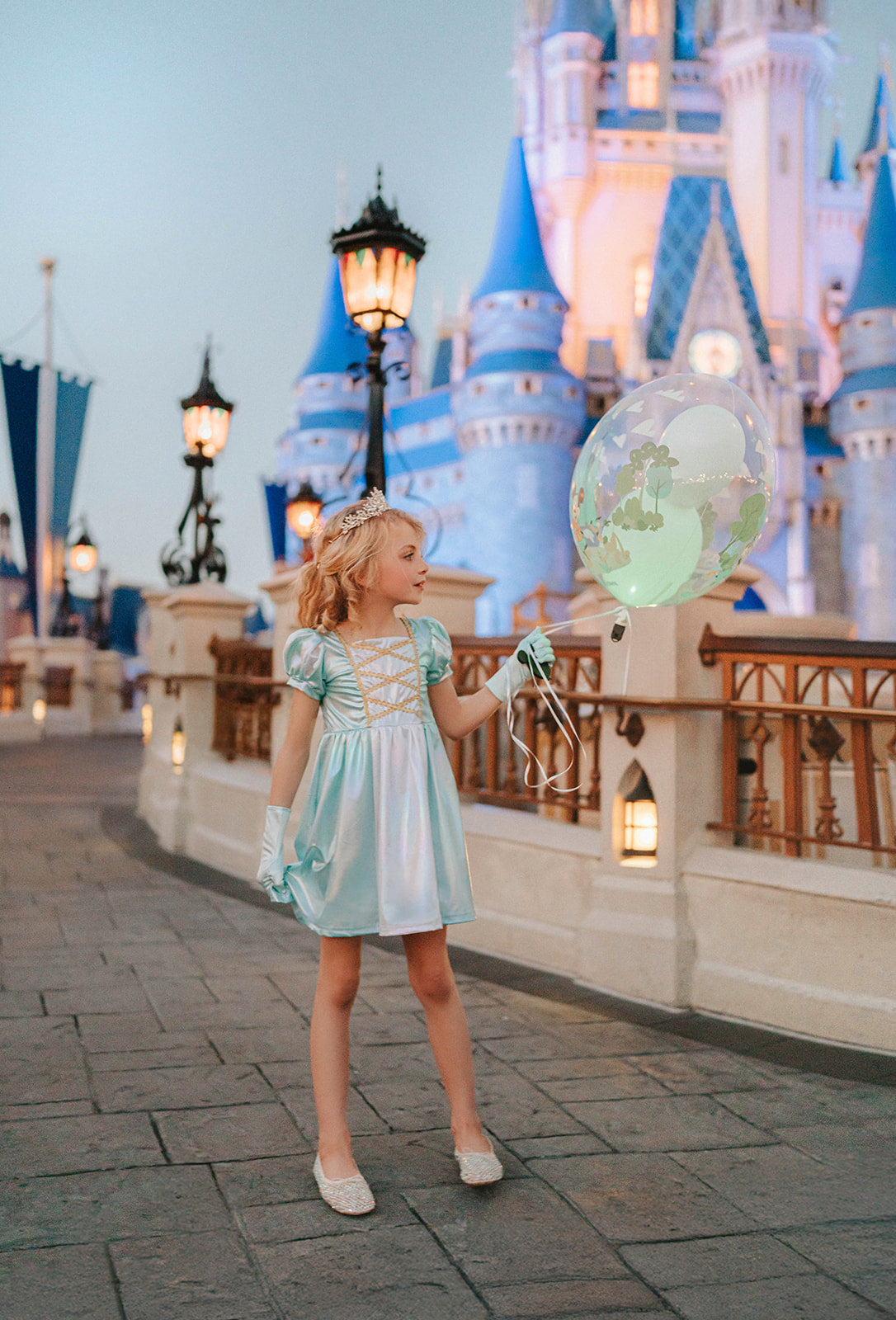 A young girls is wearing a metallic Cinderella Twirl dress. The light blue and white knee length dress has a criss cross gold ribbon across the bodice. The ballroom puff sleeves add elegance.