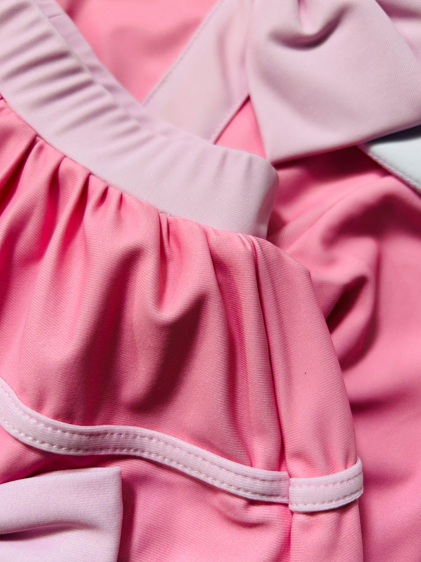 There is white collar with a pink bow at the neck. Two lighter pink stripes are on the chest like ribbon tails. The bottom is a skirt with bows light pink bows at the hem.