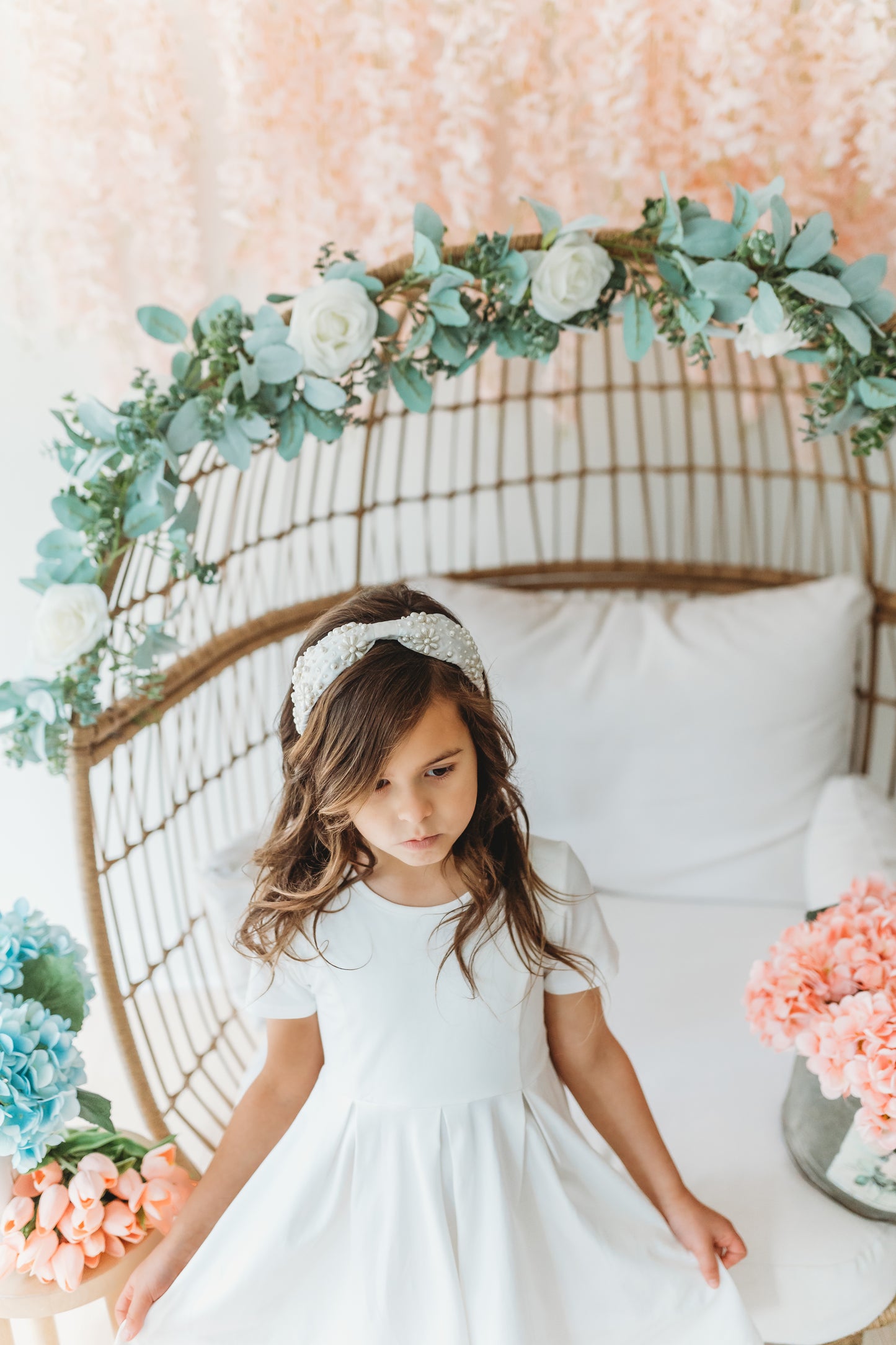 The Daisy Pearl Headband is white satin with pearls in assorted sizes. The pearls make daisy flower shapes and are spread around on both sides. This hair accessory is designed for all day comfort and is give any outfit an added touch of glamour.