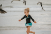 A young girl is wearing a 2 piece long sleeve rash guard swim set. The top is black with turquoise and goldenrod accents. The bottom has a turquoise ruffle over a mint teal skirt with goldenrod hem accent.