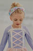 A young girl stands on a beach wearing a pastel pink and purple Rapunzel Rashguard Swimsuit, adorned with crisscross and lace detail. The bodice is lavender and skirt is light pink. The swimsuit is SPF 50 for protection from the sun.