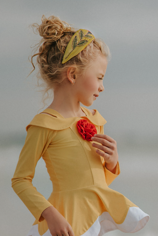 A young girl is wearing the Red Rose Rash Guard Swim Set featuring a yellow and white design with a red rose on the chest. The 2 piece swim set has long sleeves and SPF 50 for sun protection. The top flares out peplum style for the added princess ballgown effect.
