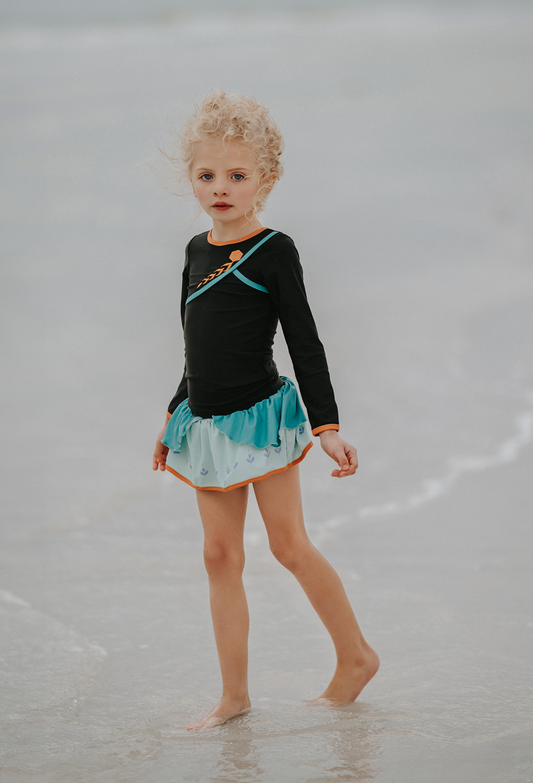 A young girl is wearing a 2 piece long sleeve rash guard swim set. The top is black with turquoise and goldenrod accents. The bottom has a turquoise ruffle over a mint teal skirt with goldenrod hem accent.