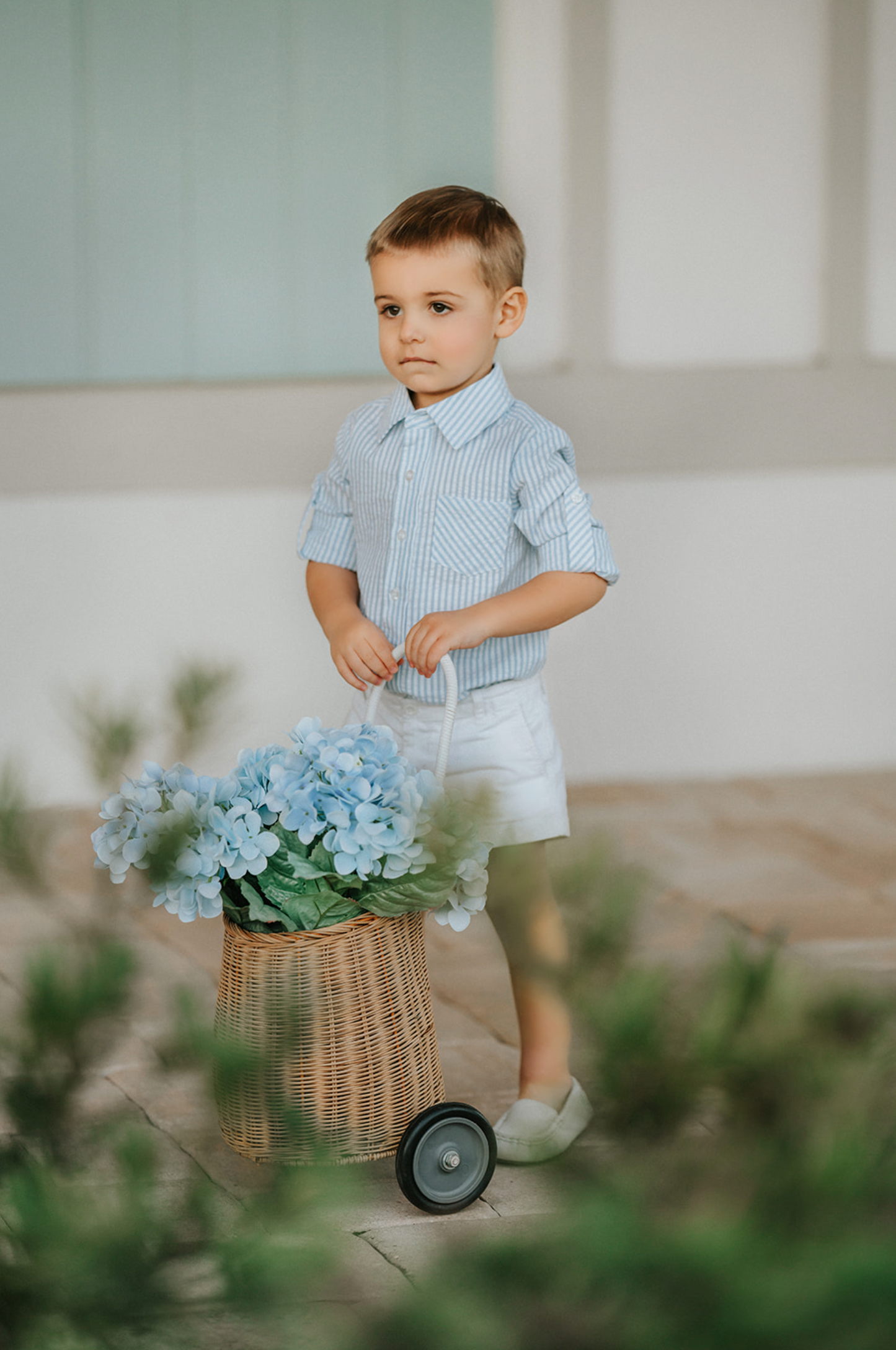 A young boy wears a long sleeve button up collared shirt. A light blue and white vertical seersucker shirt with a pocket on the left chest.