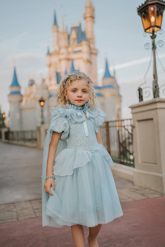 A young girl stands in a light blue gown. The chiffon puff sleeves lead into a light blue lace bodice. There is a small chiffon bustle ruffle over a tulle skirt. The skirt is lined with tulle and cotton for fullness.