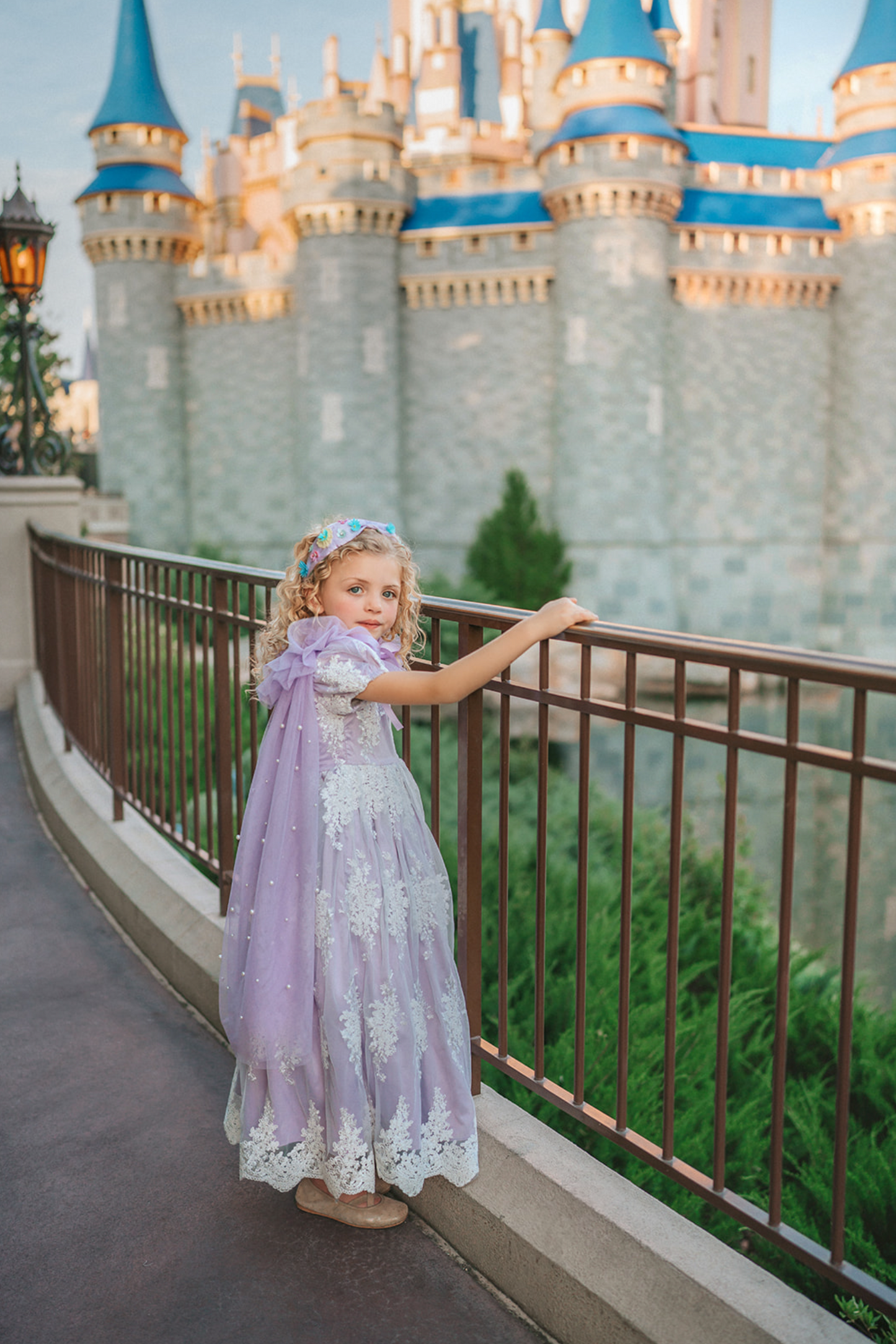 A young girl wears a soft tulle lavender cape tied at the shoulders with a satin ribbon. The cape has beautiful pearls placed all over and a ruffle collar.