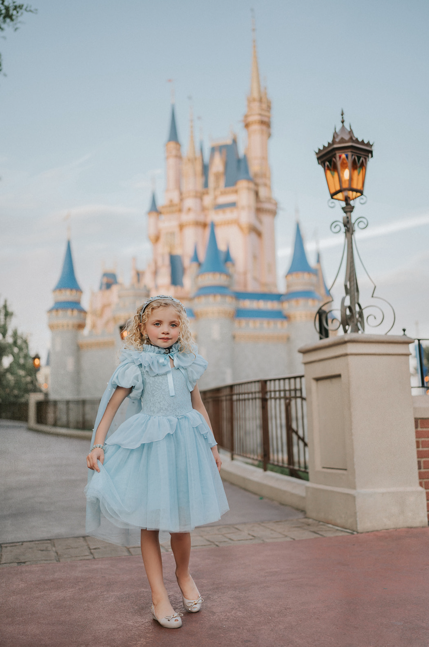 A young girl wears a soft tulle light blue cape tied at the shoulders with a satin ribbon. The cape has beautiful pearls placed all over and a ruffle collar.