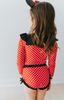 A young girl is wearing our Miss Mouse Rashguard Swim set. This 2pc swim has SPF 50. The top is red with white polka dots. There is a large black bow in the center and small ruffles on the shoulder. The bottoms have black ruffles along the edge.