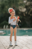 A young girl is wearing a 2 piece long sleeve rash guard swim set. The top is white with yellow on the upper chest. Across the yellow is red scrolling rick rack. The bottoms are a faux denim with black and white cow print panels.