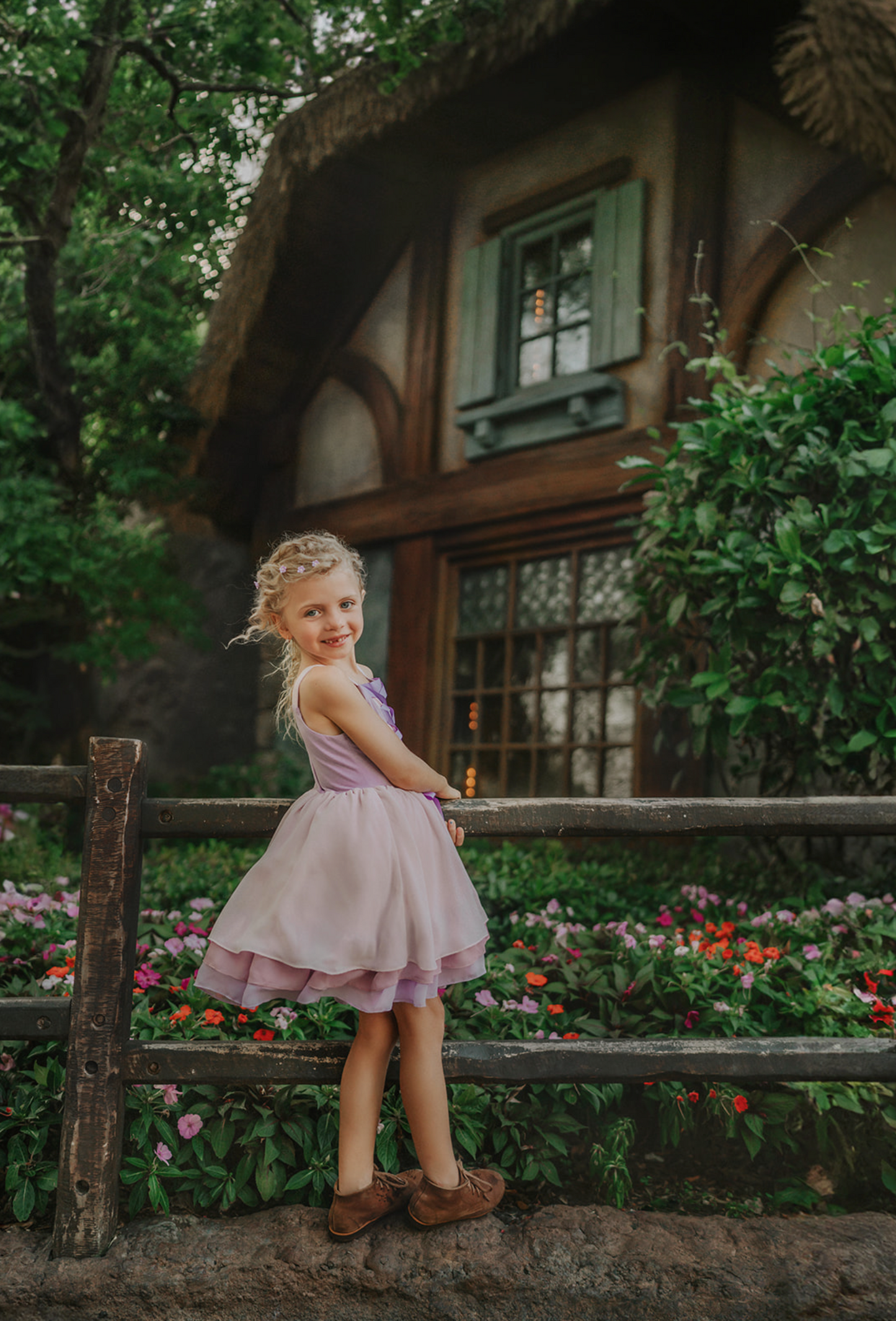 A young girl is adorned in the Portrait Petite Twirl Length Rapunzel Gown—a flowing, light violet princess dress featuring a purple ribbon corset design on the bodice. The skirts are 3 layers of light dusty purple, pink and lavender. The skirt is perfect for twirling and dancing in any enchanted land.