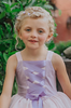 A young girl is adorned in the Portrait Petite Twirl Length Rapunzel Gown—a flowing, light violet princess dress featuring a purple ribbon corset design on the bodice. The skirts are 3 layers of light dusty purple, pink and lavender. The skirt is perfect for twirling and dancing in any enchanted land.
