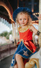 A young girl is wearing our Sorcerer Mouse Twirl Dress and Hat. That wizard hat is blue with silver moon and stars. The dress has a gold collar and red bodice. The skirt has a gold rope bow and a metallic red bustle layer atop a blue twirl skirt. The skirt is adorned with a silver moon and stars.