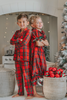 A young child in Unisex Pj's in Red Plaid decorates a Christmas tree. The plaid has green, white and black over a bright red. The classic 2 piece pajamas have green piping and red buttons down the front of the shirt.