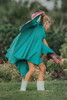 A young girl twirls in a beautiful turquoise dress. The short puff sleeves and flowing skirt look classic. There is a beautiful butterfly wing cape that attaches with buttons in the back. The butterfly has bright teal, pink and green designs on the wings.
