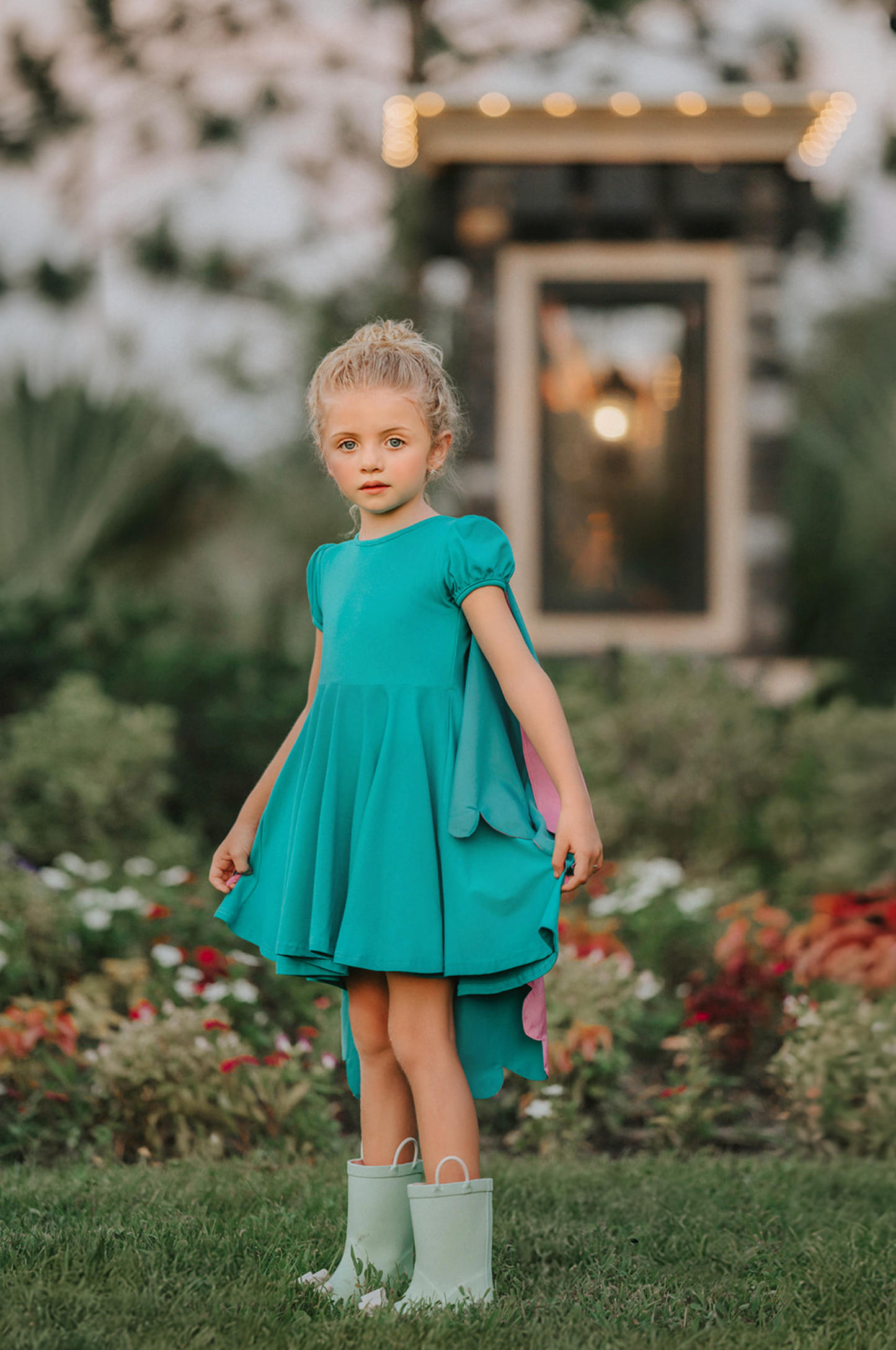 A young girl twirls in a beautiful turquoise dress. The short puff sleeves and flowing skirt look classic. There is a beautiful butterfly wing cape that attaches with buttons in the back. The butterfly has bright teal, pink and green designs on the wings.