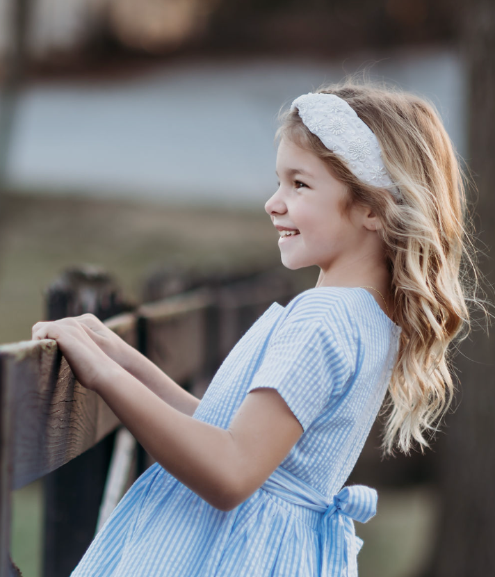 The Micro Beaded Floral Celebration Headband is white with small white white beads in various shapes. They are sewn in floral patterns and scattered to cover the headband. This hair accessory is designed for all day comfort.