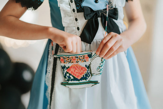 Child wearing Alice costume holding a beaded teacup-shaped purse, perfect for tea parties, dress-up, or whimsical gifts
Close-up of girl in blue and white dress with black bow, opening a colorful beaded teacup crossbody bag