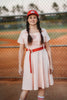 Eden is wearing the Adult Vintage Baseball Dress, styled with a red belt. The outfit is crafted from soft cotton jersey knit fabric and is available in adult sizes.