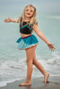 A young girl is wearing a 2 piece long sleeve rash guard swim set. The top is black with turquoise and goldenrod accents. The bottom has a turquoise ruffle over a mint teal skirt with goldenrod hem accent.