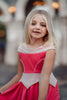 A young girl is wearing an all cotton bright pink princess twirl dress. The neckline has nude mesh and light pink sits off the shoulder. The bright pink bodice has light pink piping and leads into a light pink handkerchief band. The skirt is flowy and bright pink. A light pink ruffle at the hem line adds a beautiful twirl.