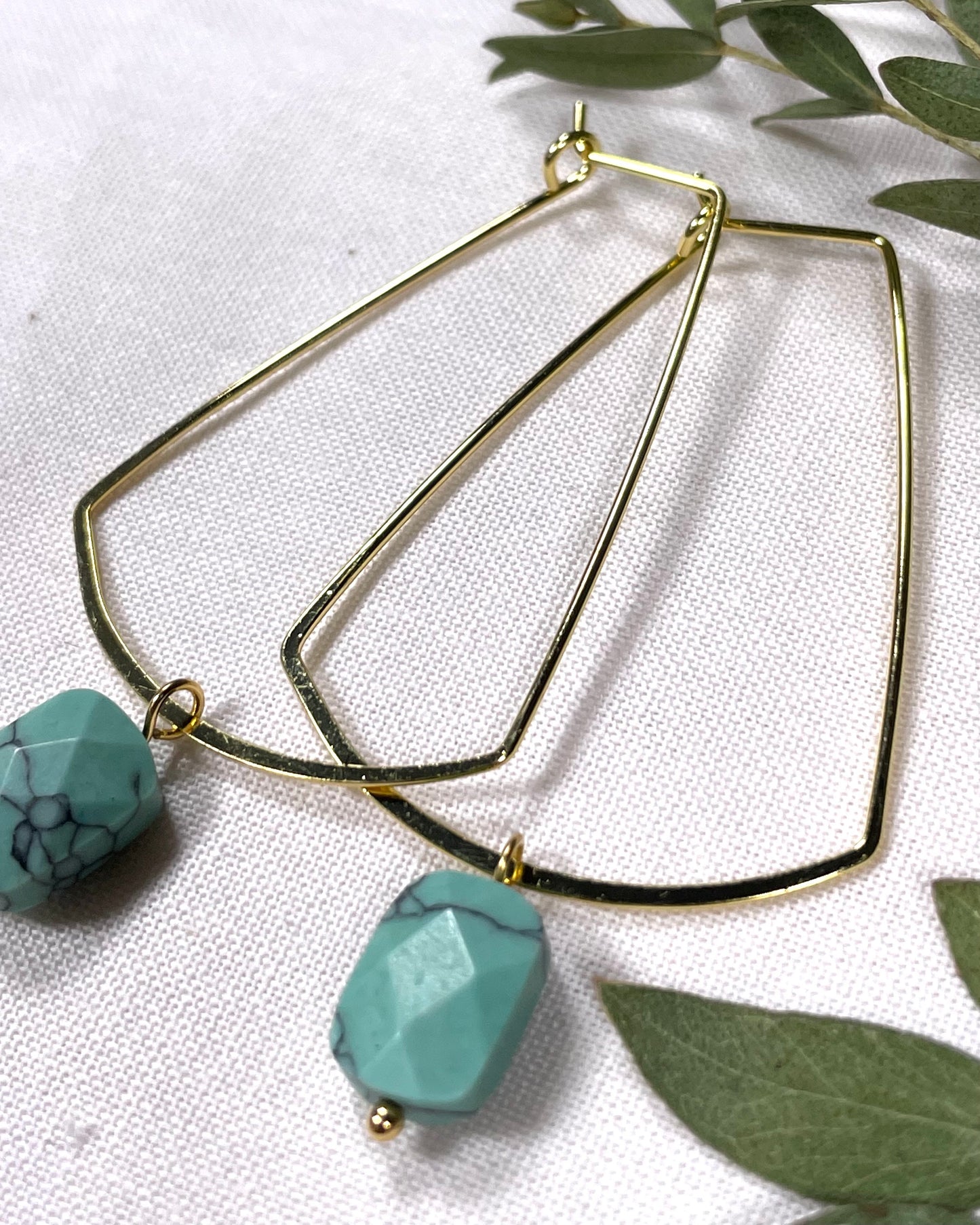 Golden hoops rectangle shape hoops with a turquoise faceted stone that dangles from the bottom.