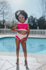 A young girl is wearing a pink 2 piece swimsuit. The Sleeping Beauty swim set has a pink collar that resembles a ballgown. The top has light pink piping and trim. The modest bottoms have a pink overlay and ruffles on the legs.