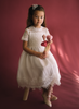 A young girl is wearing a Victorian Day Gown in White. The dress has elegant lace sleeves and lace victorian collar. A sheer white layer adds softness and flows into a wide lace hem below the knee.