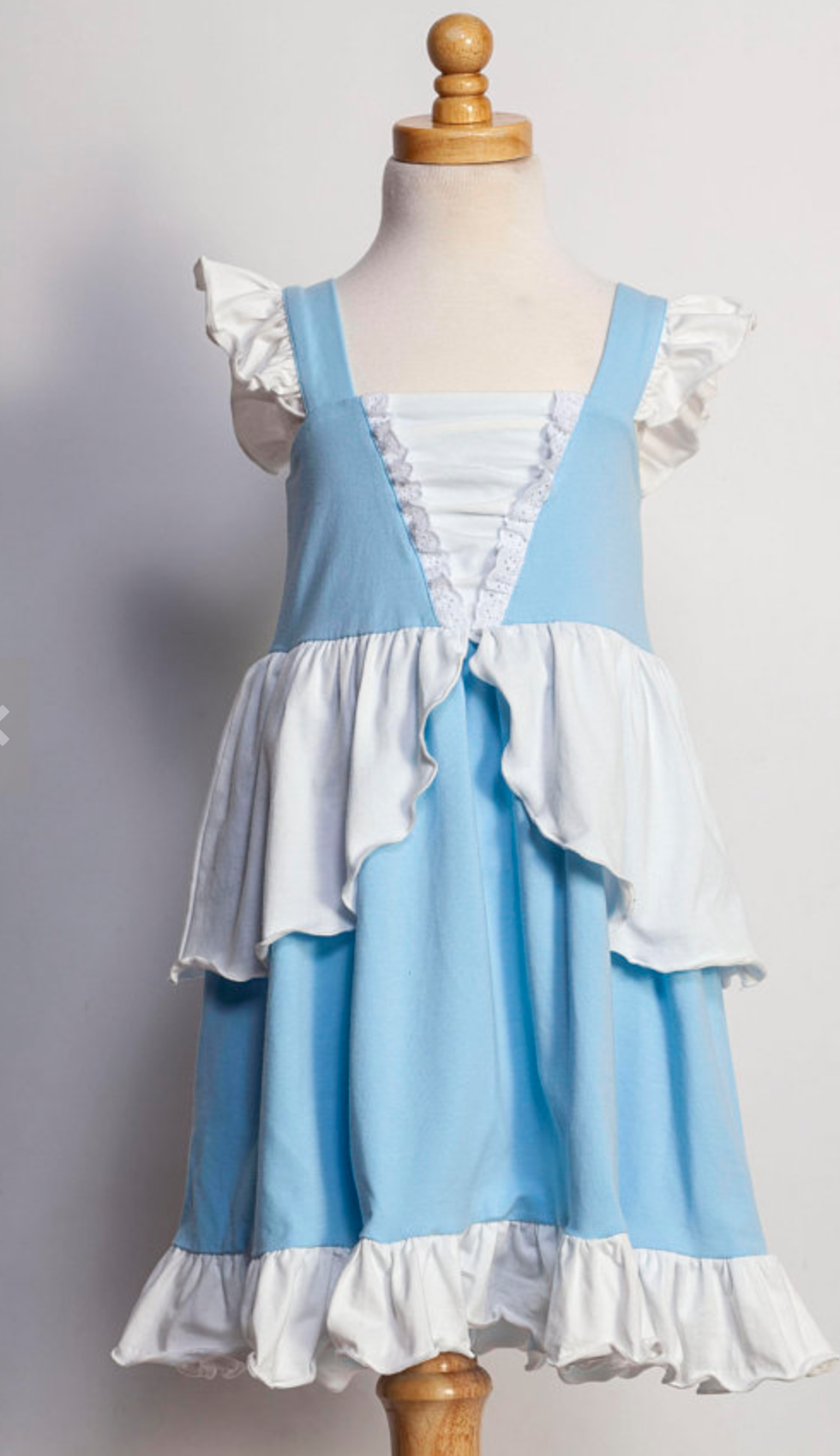 A young girl in an "Our Original Cinderella Twirl Dress" stands near a castle. The dress has a white flutter ruffle on the straps. There is a white skirt ruffle that overlays the blue twirl skirt. The soft cotton material is comfortable and breathable.