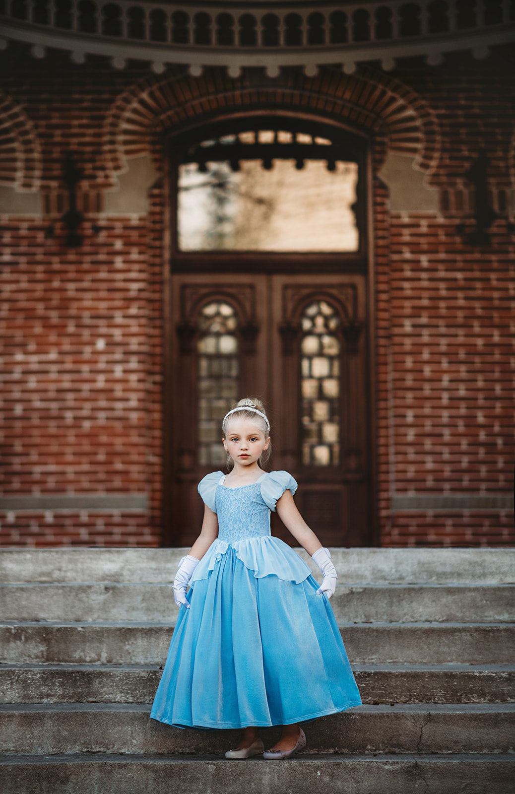 A young girl stands in a light blue gown. The chiffon puff sleeves lead into a light blue lace bodice. There is a small chiffon bustle ruffle over a stretch velour skirt. The skirt is lined with tulle and cotton for fullness.