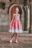 A young girl is wearing The Fairy Godmother Collection Cinderelly Pink Dress. The dress is woven cotton with a white collar and pink bow. The full skirt has bows at the bottom with a white hem.