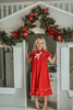 A young girl is wearing The Original Clara Nutcracker Gown in red, featuring red ruffles and a white bow. The buttery soft fabric is cozy and sensory friendly. The puff sleeves with ribbon detail and the ruffles at the hem add a traditional classic look.