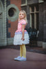 A young girl is wearing true pink and lavender bodice and white petal skirt dress. The top has puff sleeves and ruffled collar. The white skirt imitates feathers and is lined with tule and cotton to give a fuller appearance.