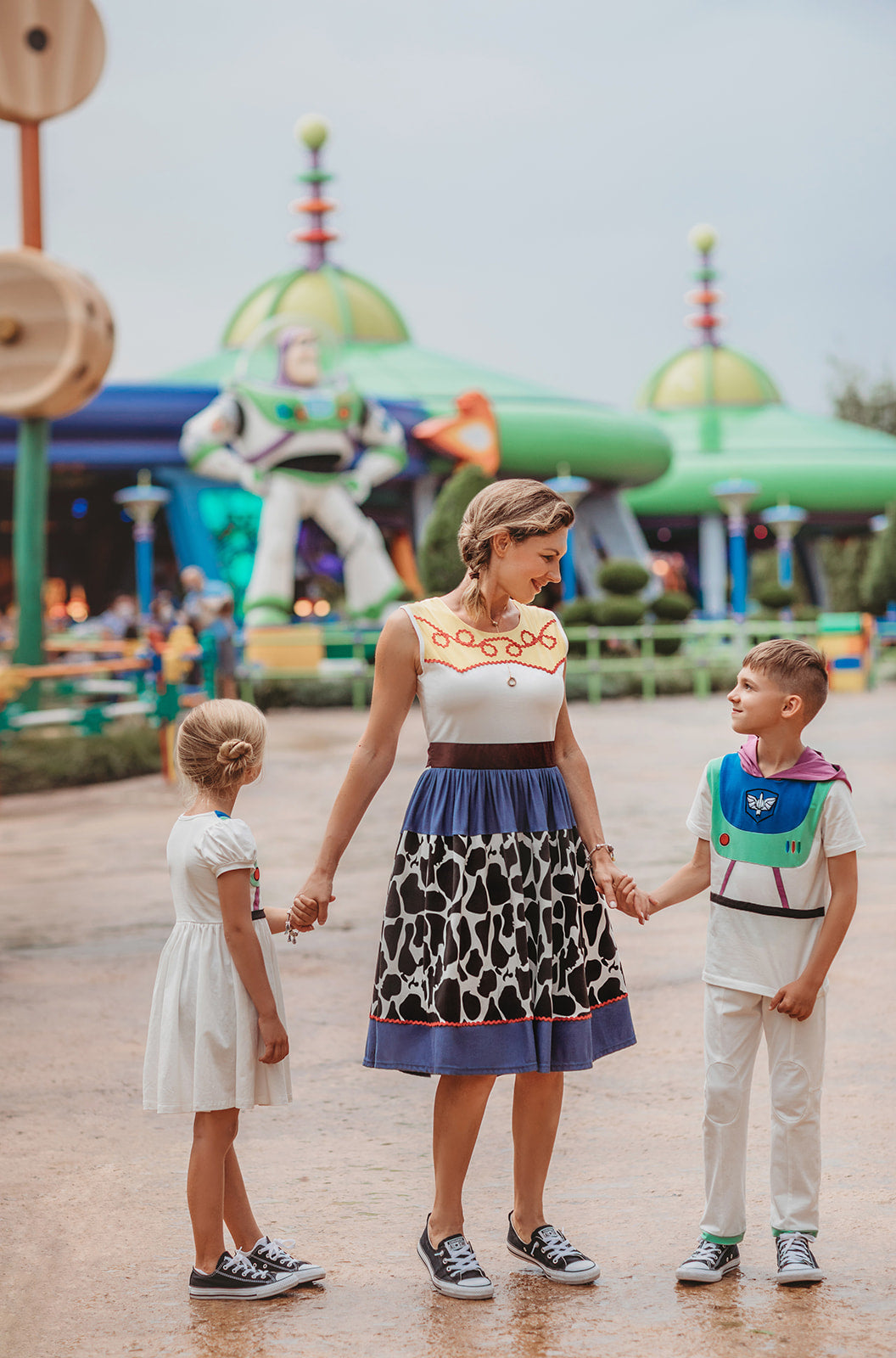 A young boy is wearing a purple hood attached to a white t-shirt. There is blue and green on the chest of the shirt with purple lines and a black band along the waist resembling an astronaut. There is an embroidered white symbol, red circle and red, blue and green lines that resemble space suit buttons.