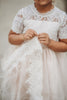 A young girl is wearing a Victorian Day Gown in Ivory. The dress has elegant lace sleeves and lace victorian collar. A sheer white layer adds softness and flows into a wide lace hem below the knee.