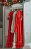 A young girl is wearing The Original Clara Nutcracker Christmas Gown Long Sleeve in Red, adorned with a white bow. There are two buttons on the next with a ruffle at the top. There is one ruffle at the bottom of the sleeve and two ruffles at the bottom of the gown. Buttery soft polyester knit fabric.
